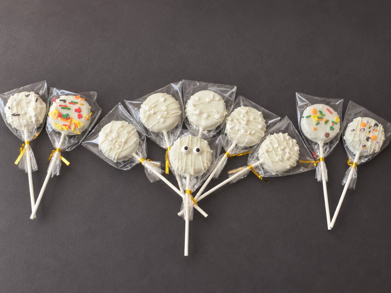 A fan of wrapped cookie pops with white decorations, candy eyes and autumn sprinkles.