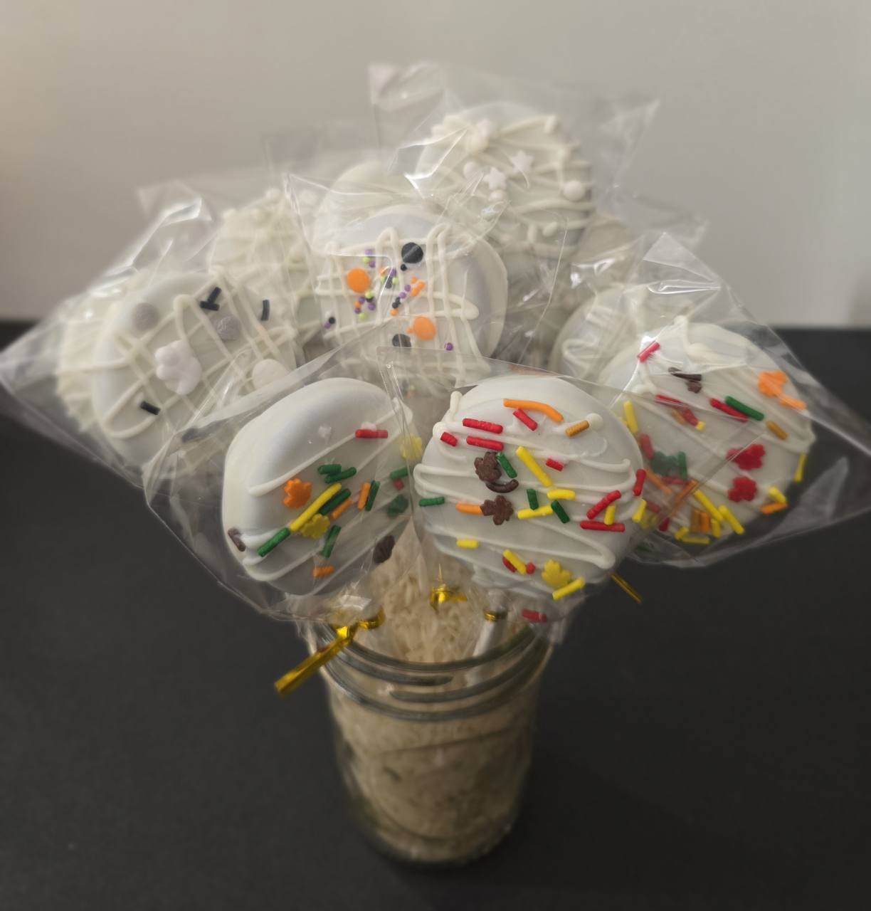 Close-up of dipped cookie pops with colorful leaf sprinkles and white drizzle.